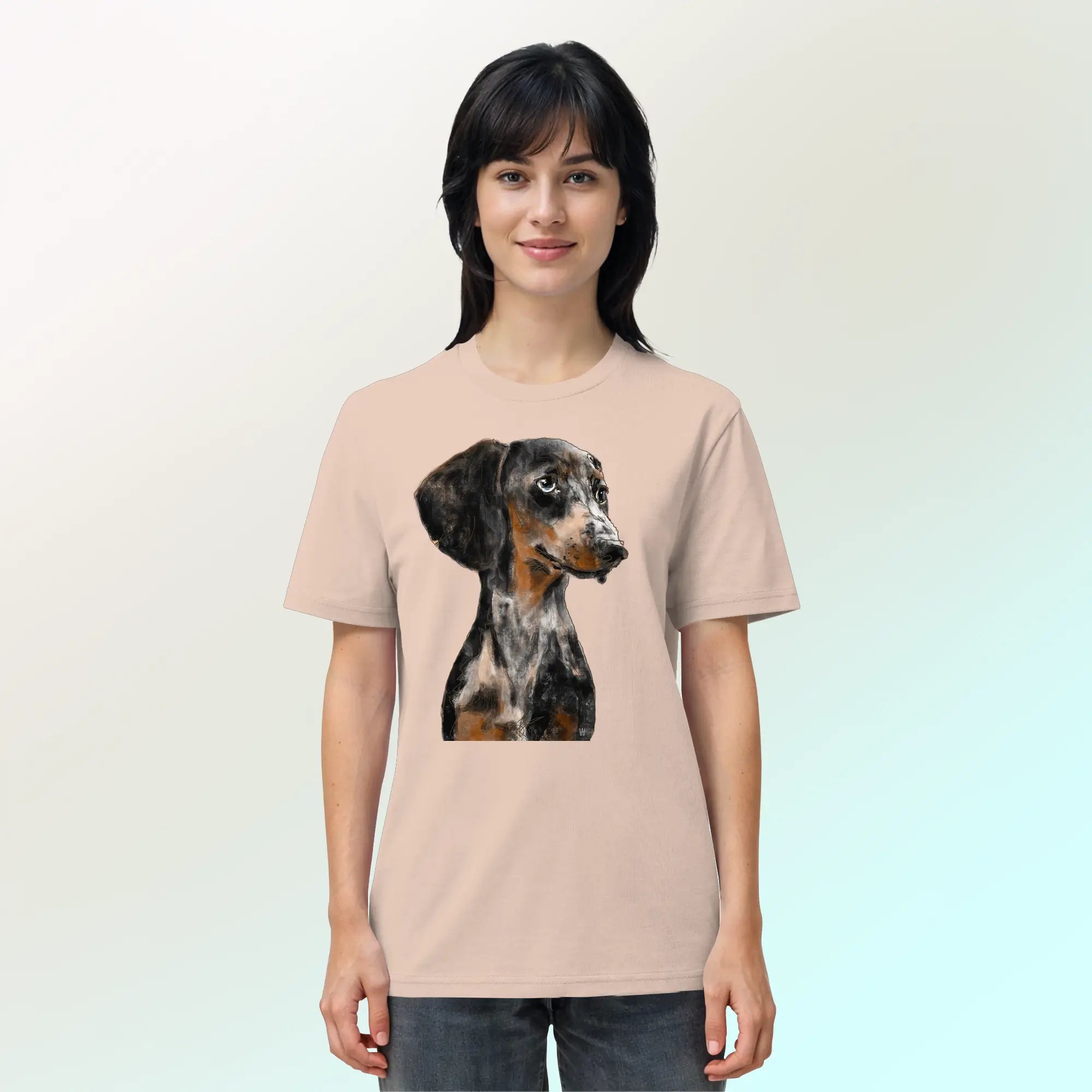 Junge, hübsche Frau trägt ein Bio-T-Shirt in Pfirsichrosa mit handgezeichnetem Dackel-Motiv "Klugi".
