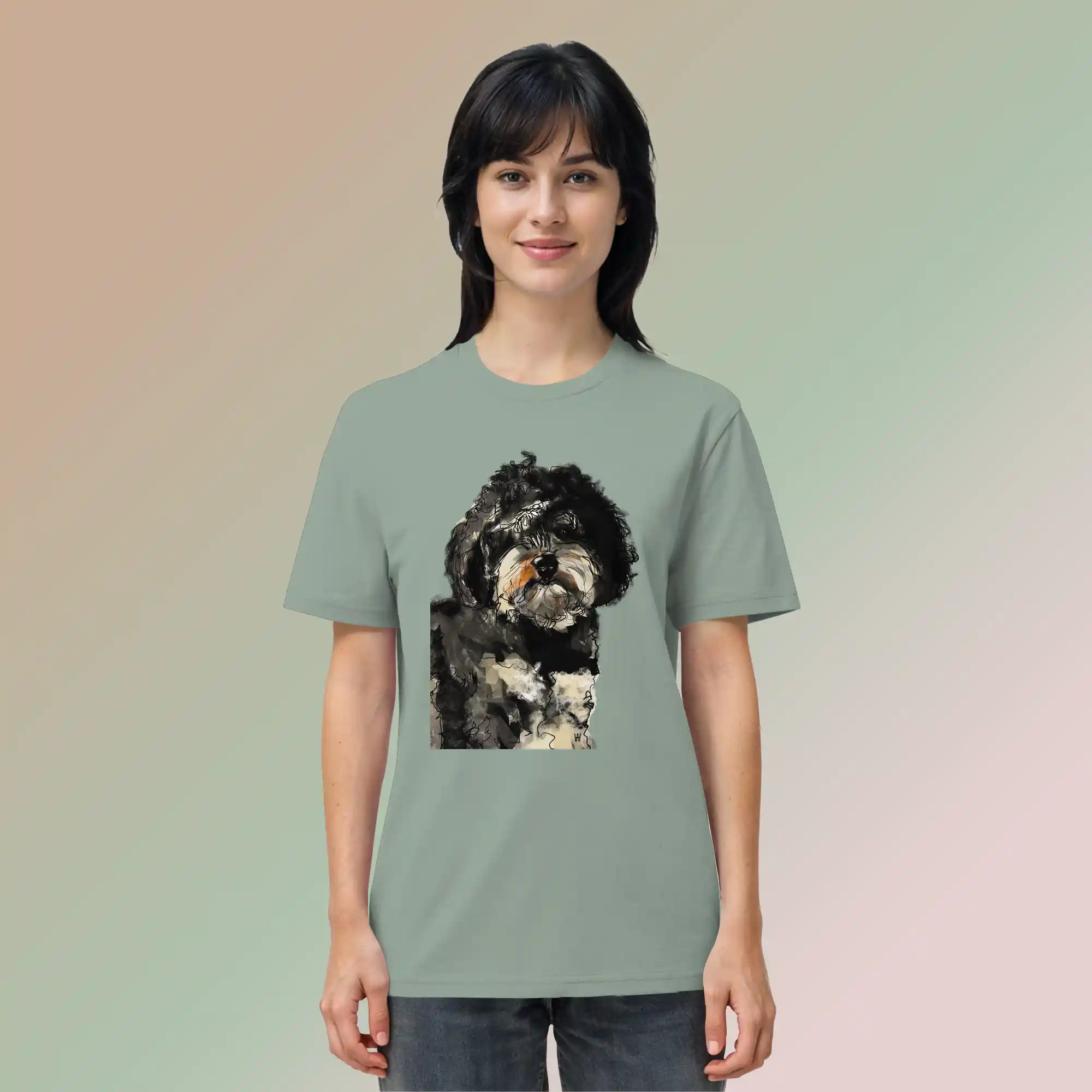 Junge, hübsche Frau trägt handgezeichnete Havapoo-Illustration "Wuschel" auf einem salbeigrünen Bio-T-Shirt vor einem zarten Farbverlauf.